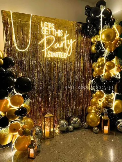 A classic black and gold party theme is always a winner. This setup features a gold fringe backdrop, a 'Lets Get This Party Started' neon sign, and a dramatic black and gold balloon garland.