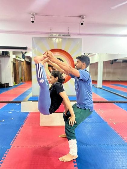 A standing partner stretch that helps to deepen the forward fold and release the hamstrings. The partner provides gentle assistance to help the student find more length in their spine.