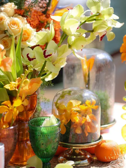 A close-up of the vibrant tablescape, with flowers under glass domes, orchids, and colorful glassware creating a fresh and tropical feel.