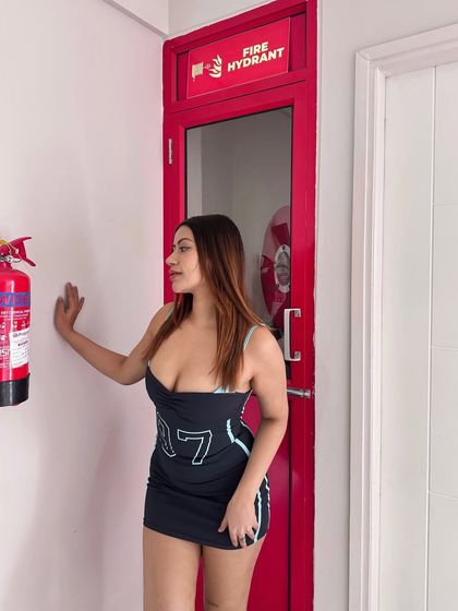 Leaning against a red door in the sporty mini dress, showing a fun, casual party style.