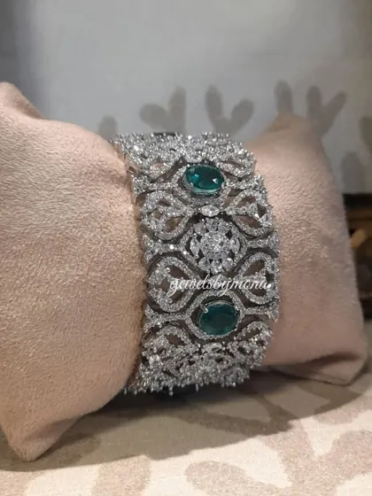 This wide diamond bracelet, accented with deep green emeralds, is a statement of pure luxury. The intricate lattice design is studded with brilliant diamonds, making it a perfect centerpiece for a bridal or formal ensemble.