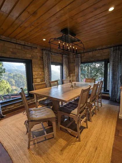 A full view of the dining room, showcasing the long wooden table perfect for family meals, the industrial-style chandelier, and the incredible mountain views from every window.