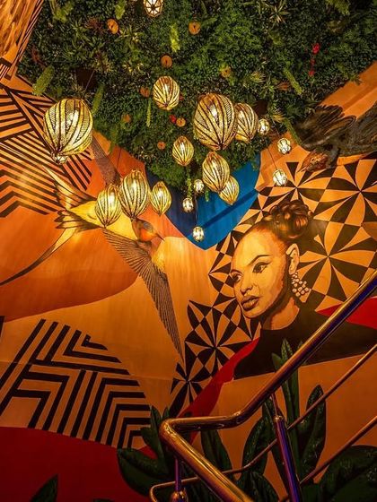 A detail of the vibrant mural and lighting on the staircase at 'Highdrate.' The artwork combines geometric patterns and figurative elements, creating a rich visual tapestry that is central to the space's identity.