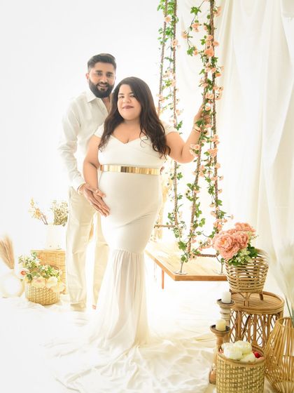 A lovely couple's portrait in matching white outfits. The mom-to-be stands by our floral swing in a beautiful white gown, creating a bright and angelic scene.