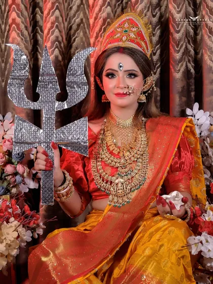 A majestic portrait of the model as Durga, holding a trishul against a backdrop of flowers.