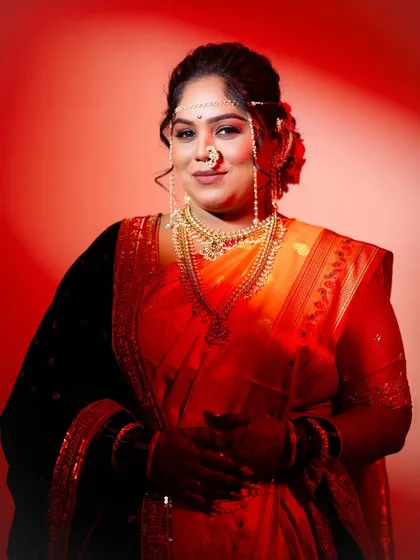 A classic portrait of a Maharashtrian bride against a bold red background. Her traditional jewelry and serene expression are the focus of this striking image.
