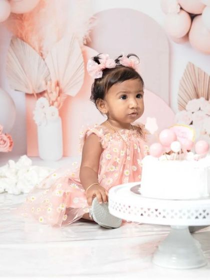 A sweet one-year-old girl enjoying her pink-themed cake smash session. I love capturing these close-ups of their frosting-covered fingers and happy faces.