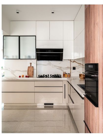 The kitchen in the Kanasu project is clean and modern, with glossy white and beige cabinets, a white marble backsplash with gold veining, and sleek black hardware. The design is both beautiful and highly functional.