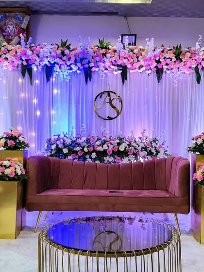 This elegant reception stage features a soft, romantic aesthetic. A floral arch of pink and white roses sits above a backdrop of white curtains and subtle lighting, with a custom monogram adding a personal touch for the couple.