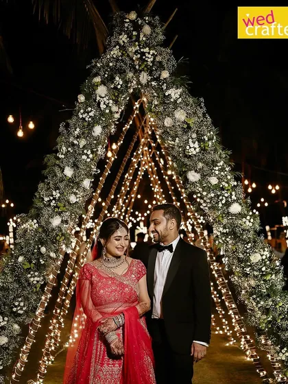 A magical moment as the couple walks through a teepee arch adorned with white flowers and wrapped in twinkling fairy lights at their beach reception.