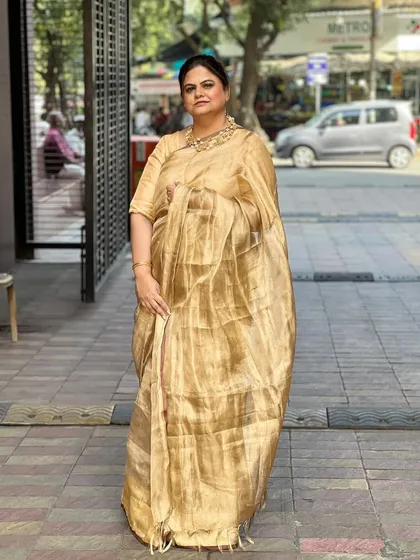 A client looking graceful in a golden tissue saree. Her hair is styled in a neat, classic bun.