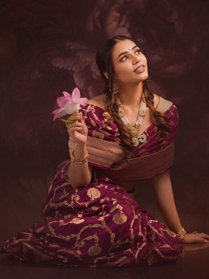 The beautiful actress Sapthami Gowda looks radiant in our deep purple Banarasi saree, holding a lotus flower in this artistic portrait.