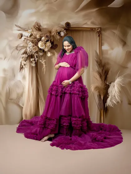 A solo portrait of the mom-to-be cradling her bump in a stunning ruffled magenta gown. The earthy, floral backdrop adds a rustic yet glamorous feel to this elegant maternity photo.