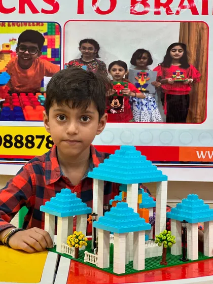 A student presents his elegant LEGO gazebo structure with a blue-tiled roof.