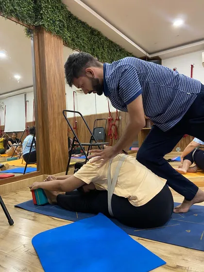 A hands-on adjustment in a seated forward bend. The strap helps the student engage their back muscles, while my guidance ensures they are folding safely and effectively.