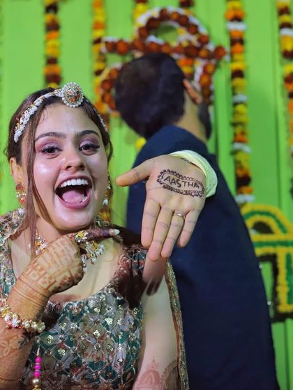 The bride playfully shows off the groom's name written on her hand with mehendi.