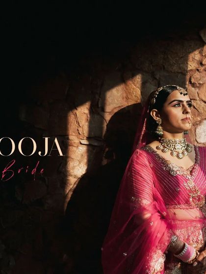 A beautiful portrait of the bride, her pink lehenga glowing in the sunlight, framed by a stone wall.