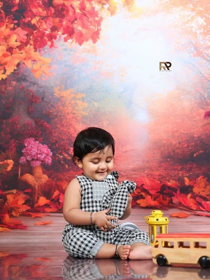A baby in a checkered outfit plays with toys in the autumn forest setting. The warm and vibrant colors create a cozy and magical feel.