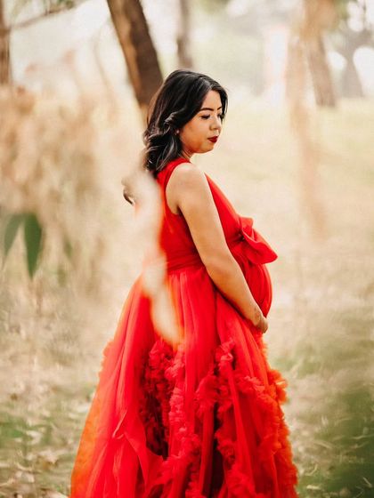 An artistic outdoor portrait with foliage in the foreground, creating a natural frame around the expecting mother in her red gown. This technique adds depth and a sense of privacy to the image.