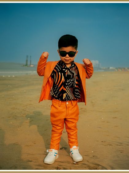 Confidence looks good on him. This custom orange suit, paired with a cool printed shirt and sunglasses, shows how we can create a complete, head-turning look for your boy's special day.