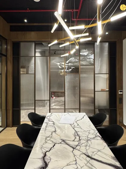 The main boardroom at 'Project LH.' A dramatic marble table and sculptural light fixture create a powerful focal point, while fluted glass partitions provide privacy without completely closing off the space from the rest of the office.