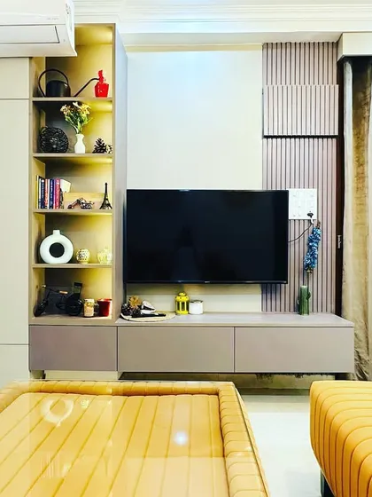 This living room features a custom-designed TV unit that maximizes storage and style. The unit includes a tall cabinet, open display shelves, and a low console, all finished in a sophisticated two-tone palette with fluted panel accents.