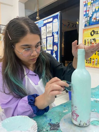 A participant in our bottle decoupage workshop carefully applies paint to a glass bottle. This is a wonderful way to learn upcycling and turn an ordinary object into a decorative piece for your home.
