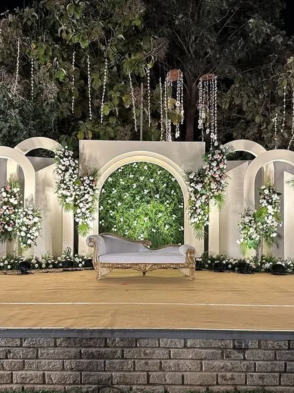 Modern, minimal, and absolutely elegant. This outdoor stage design uses clean white arches, a lush greenery wall, and soft florals to create a sophisticated backdrop that feels both grand and serene.