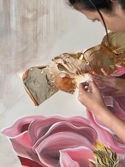 The delicate process of applying gold leaf to the 'Native Grace' mural. The warm glow of the gold adds a layer of elegance and light to the floral composition.
