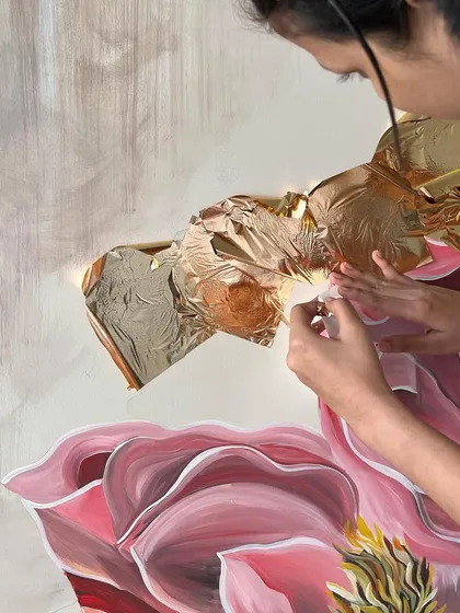 The process of applying rose gold leaf to the 'Native Grace' floral mural. This adds a warm, metallic shimmer that contrasts with the painted petals.
