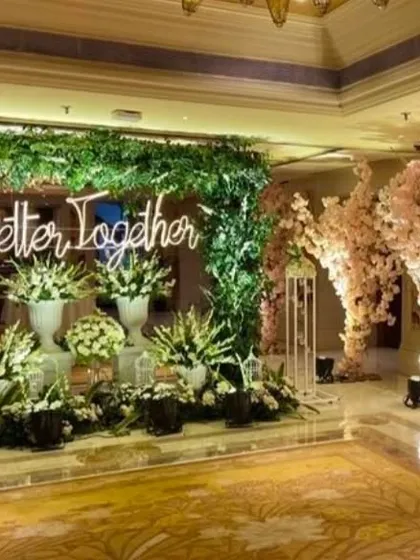 A close-up of the 'Better Together' neon sign against a lush green backdrop. This photo corner is decorated with large white floral arrangements, creating a fresh and romantic spot for pictures.