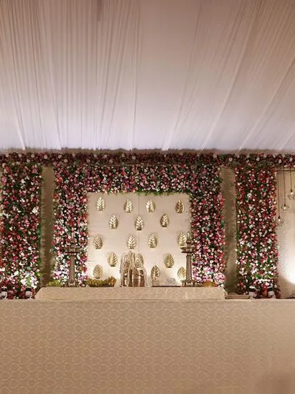 A wide-angle view of a grand indoor wedding stage, showcasing the expansive floral decor and cream-and-gold theme that creates a regal atmosphere.