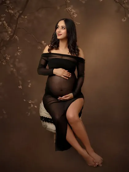 A moody and elegant portrait in a sheer black off-the-shoulder dress. The lighting highlights the beautiful silhouette against a dark, textured background.