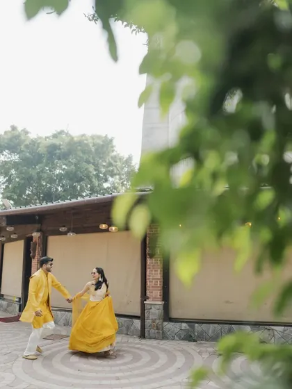 A candid shot of the couple enjoying a dance during their Haldi celebration, framed by lush green leaves.