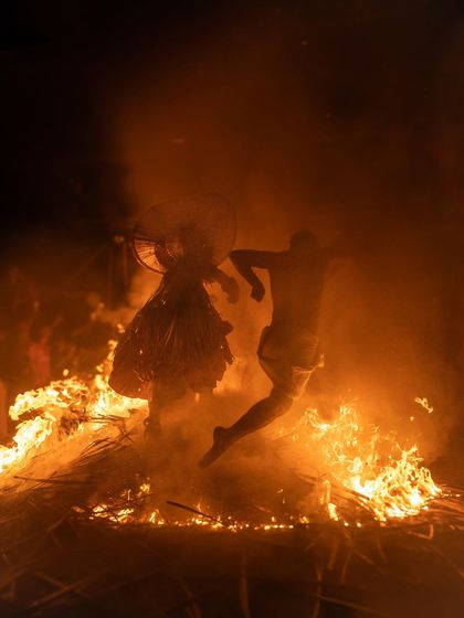 A Theyyam performer in Kerala leaps over a bonfire. This action shot captures the peak of the ritual, a moment of daring and complete surrender to the divine.