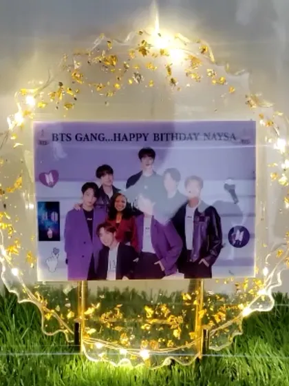 A light-up photo frame for a K-pop fan, featuring a picture of the band BTS. The gold foil and lights make it a perfect piece of fan memorabilia.