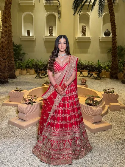 A regal portrait. The bride stands in a beautiful courtyard, her red lehenga and diamond jewellery complemented by a makeup look that is both classic and contemporary.
