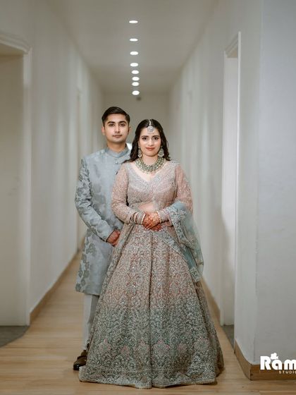 A full-length portrait of the couple in a modern, well-lit corridor. Their coordinated pastel outfits look elegant and sophisticated.