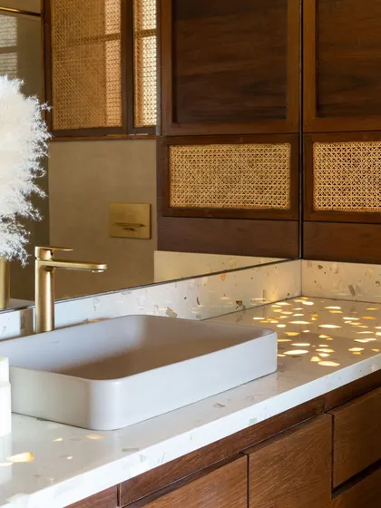 It's all in the details. For our own penthouse, we played with textures and light, seen here as sunlight dapples across the terrazzo countertop, highlighting the warmth of the wood and cane weave details in the bathroom.