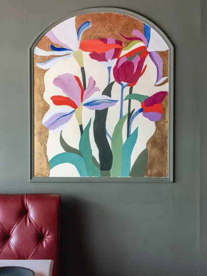 A finished view of an arched floral panel in a restaurant, featuring stylized irises and tulips against a gold leaf background. The artwork adds a touch of elegance and color to the dining space.