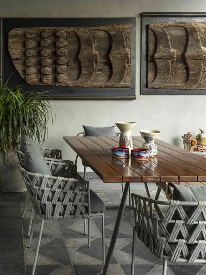 The terrace dining area at the Bammi Residence, designed for alfresco meals. The space features woven chairs and a simple wooden table, set against a backdrop of reclaimed wood art panels.