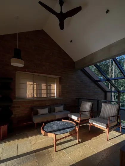 A cozy seating area with a high, slanted ceiling and a large glass window looking out into the forest. The warm sunlight and natural materials create an inviting space to relax and enjoy the view.