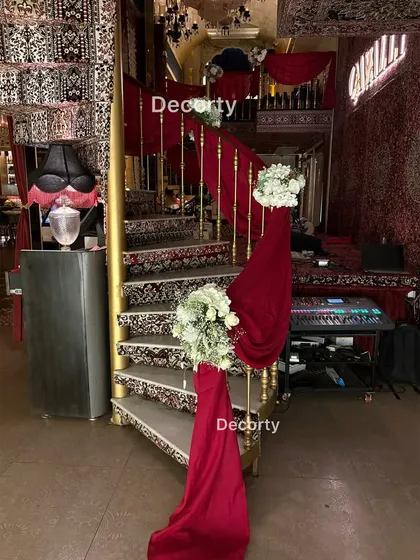 The staircase at an anniversary party, decorated with rich red velvet drapes and white floral bouquets. I style the entire venue to create a cohesive and luxurious atmosphere.