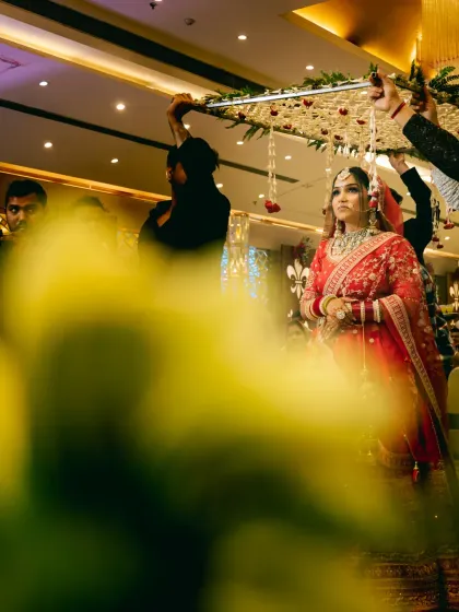 A creative shot of the bridal entry, framed by foreground elements to add depth and focus on the bride as she walks under the phoolon ki chadar.