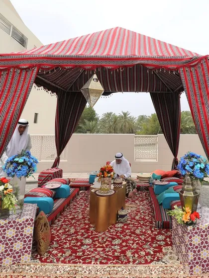 A traditional Moroccan-style tented seating area, complete with low cushions, patterned rugs, and a brass lantern, set up for a destination wedding event in Bahrain.