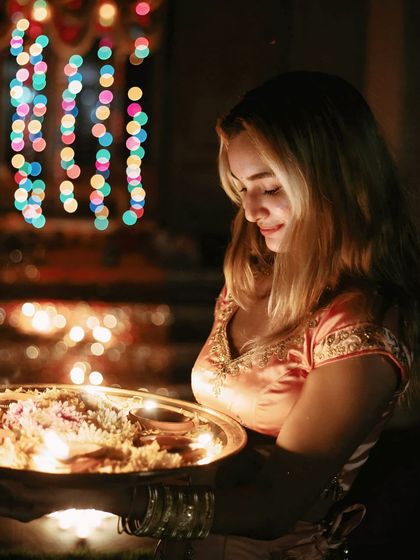 A portrait of a woman holding a thali of diyas, her face illuminated by their warm glow, embodying the grace and devotion of Dev Deepawali.
