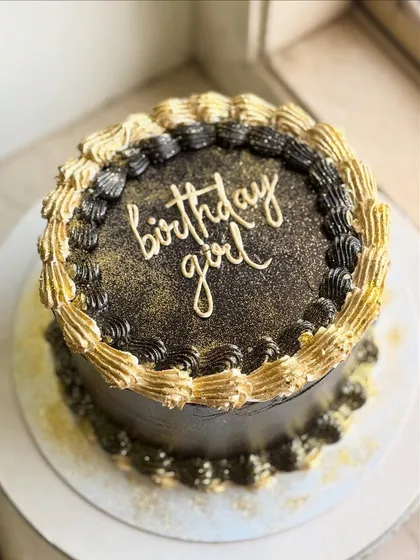 The full view of the black and gold "birthday girl" cake, showing the contrast of the gold glitter against the dark frosting.