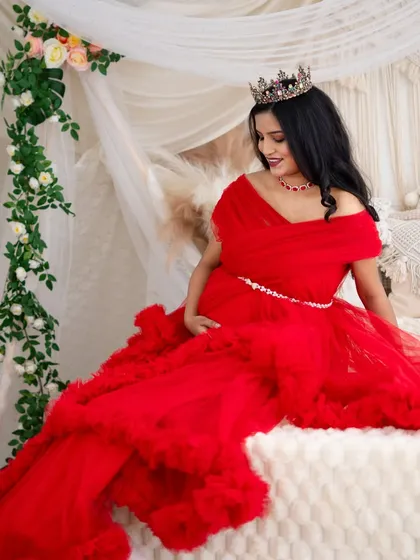 A fairytale scene on our studio bed setup. The mom-to-be, dressed in a magnificent red gown and crown, looks down at her bump with a gentle smile.