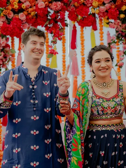 Pure happiness and victory signs from the happy couple during their Mehendi ceremony. Their vibrant, colorful outfits perfectly match the joyous mood of the event.