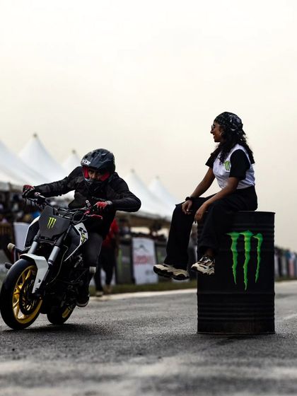 A stunt rider on a KTM Duke, with a model sitting on a Monster Energy barrel, creating a cool and edgy photo op.
